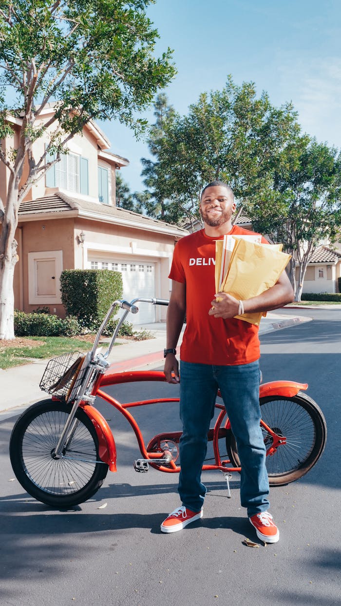 Smiling deliveryman with a red bicycle holding packages outdoors on a sunny street.